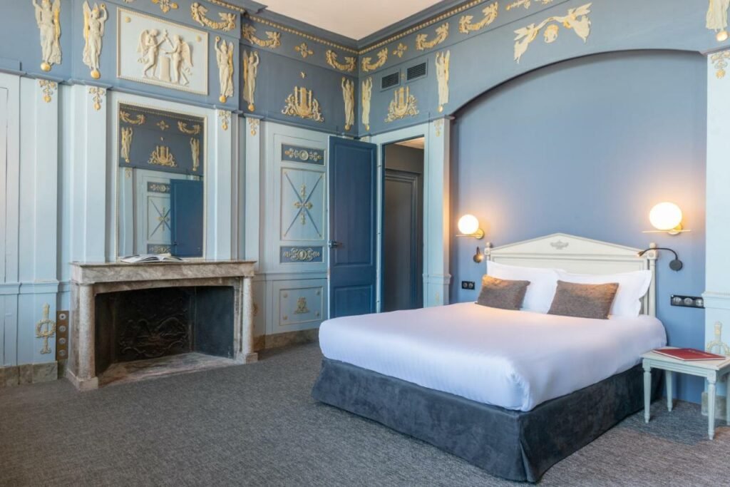 Quarto do Hôtel Anne d’Anjou, The Originals Collection com cama de casal do lado direito da imagem, do lado esquerdo da cama uma cômoda e do lado direito da cama uma lareira. Representa hotéis no Vale do Loire.