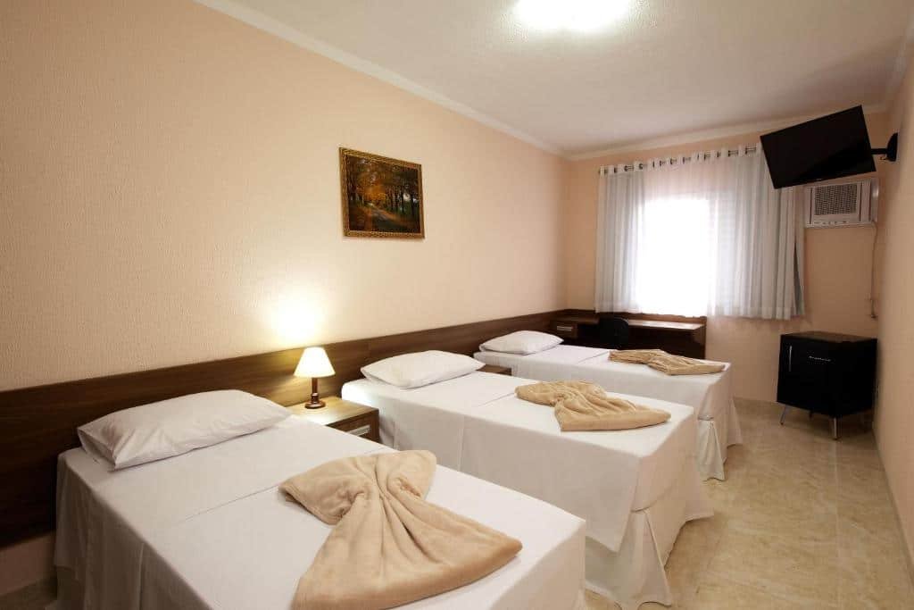 Quarto do Hotel Itupeva Terrace Residence SPA com três camas de solteiro, um frigobar, uma televisão e uma janela com cortinas, para representar hotéis perto do Hopi Hari