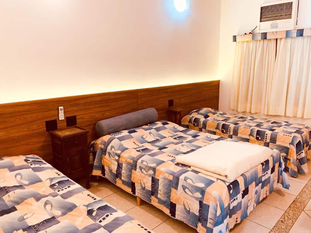 Quarto do Parque Hotel Holambra com cama de solteiro do lado direito, uma cômoda de madeira ao lado, cama de casal do ao meio e do lado esquerdo cama de solteiro.