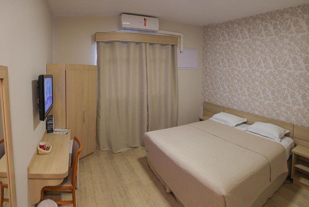 Quarto do Hotel Serra de Jundiaí com cama de casal, chão de madeira, bancada com cadeira, televisão e um armário
