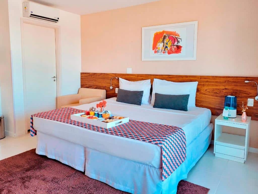 Quarto no Hplus Vision Executive com uma cama de casal, uma tapete, um ar-condicionado, uma cabeceira com luminárias e uma poltrona