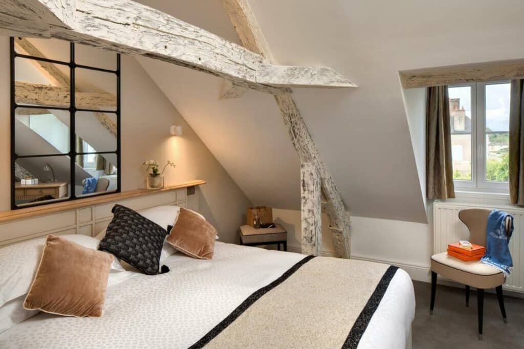 Quarto do Le Manoir Les Minimes, com cama de casal do lado esquerdo da imagem e do lado esquerdo da cama uma cadeira.  Representa hotéis no Vale Loire.