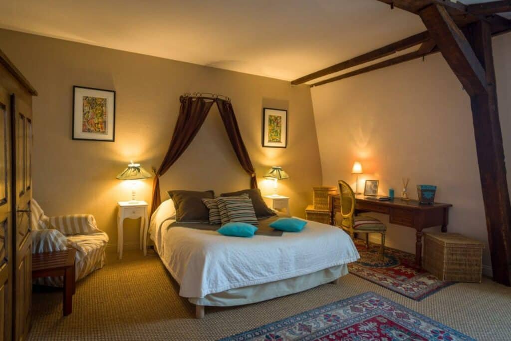 Quarto do Le Patio & Spa com cama de casal no centro com uma cômoda deem cada lado da cama com luminária e do lado esquerdo uma mesa de trabalho. Representa hotéis no Vale Loire.