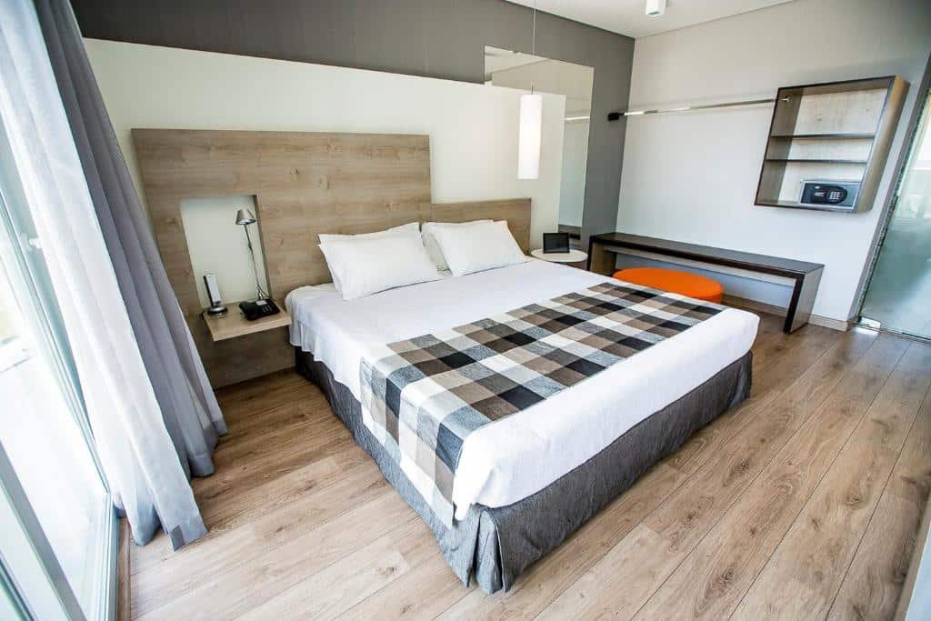 Quarto amplo do Manhattan Plaza com chão de madeira, cama de casal, espelho, um banco e um bufe, um armário de conceito aberto e uma varanda, para representar hotéis perto do consulado americano em Brasília