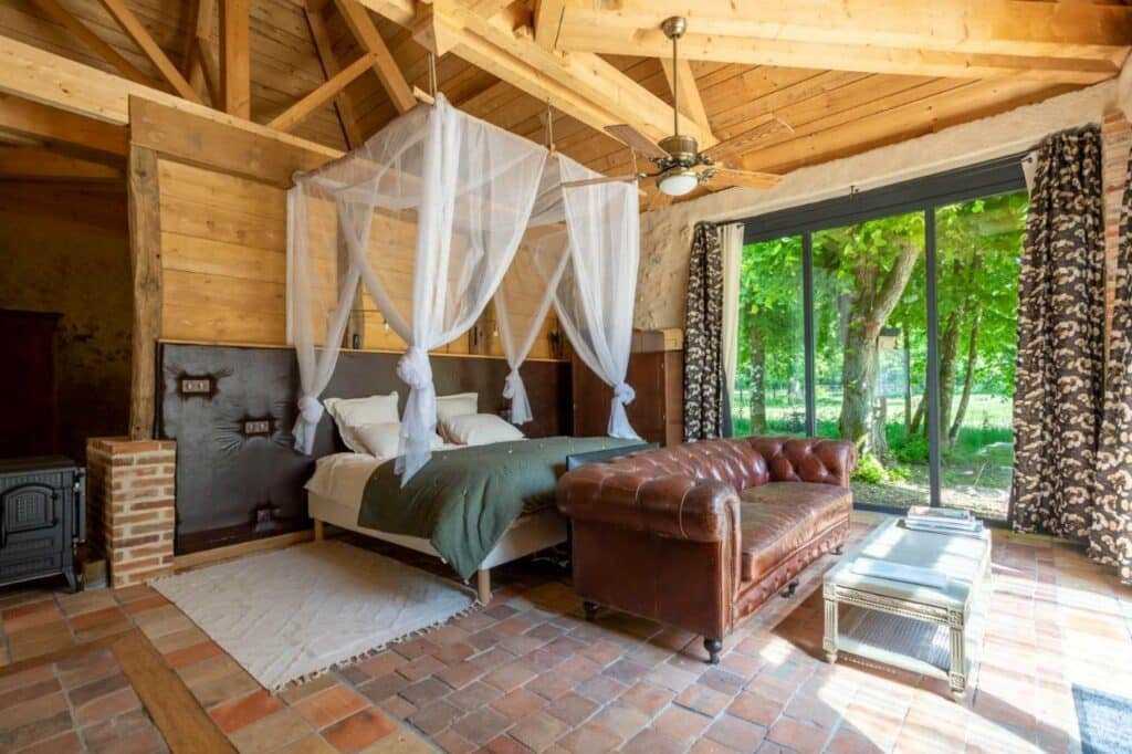 Quarto do Manoir de la Mazeraie lodge de luxe Loire Valley com cama de casal do lado esquerdo da imagem no centro do quarto com um sofá no pé da cama e uma mesa de centro a frente.