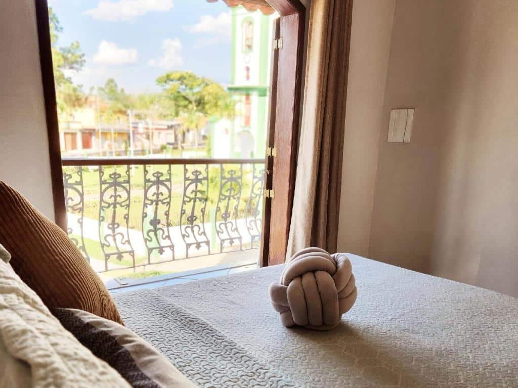 Quarto do PousaDinháChica Hospedagem com cama de casal do lado esquerdo da imagem e do lado esquerdo da cama uma porta com acesso a varanda.