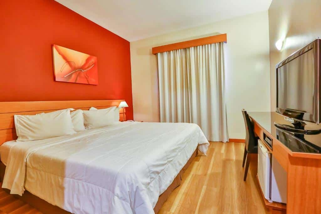Quarto do Red Roof Inn Jundiaí com uma cama de casal, chão de madeira, bancada de trabalho com cadeira, uma televisão e um frigobar