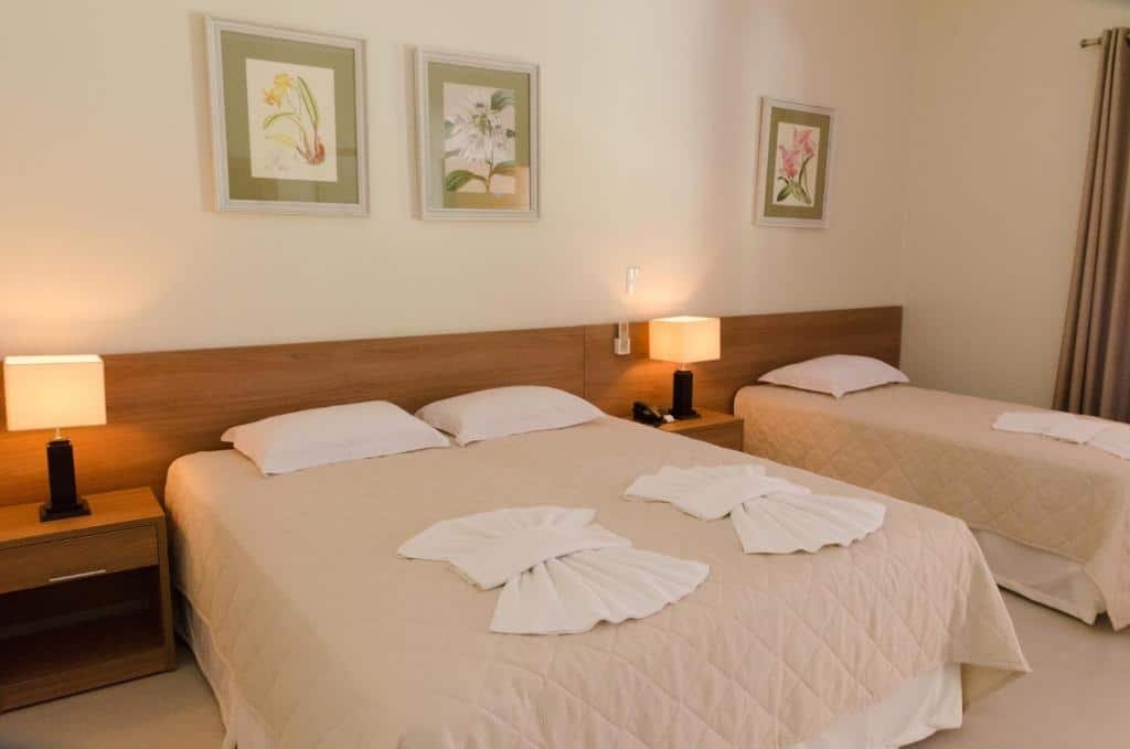 Quarto do Villa de Holanda Parque Hotel com cama de casal do lado direito com duas luminárias do lado da cama e uma cama de solteiro do lado esquerdo.