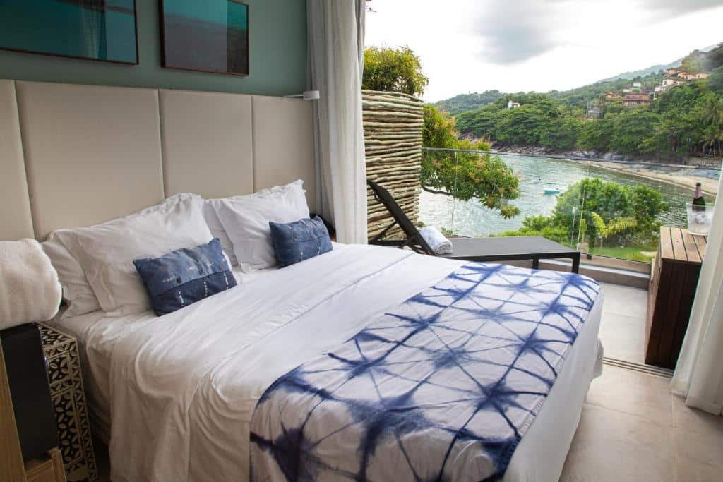 quarto no Wyndham Ilhabela Casa Di Sirena com uma cama de casal, uma ampla varanda com vista direta para a praia e uma espreguiçadeira preta com uma toalha nesta varanda