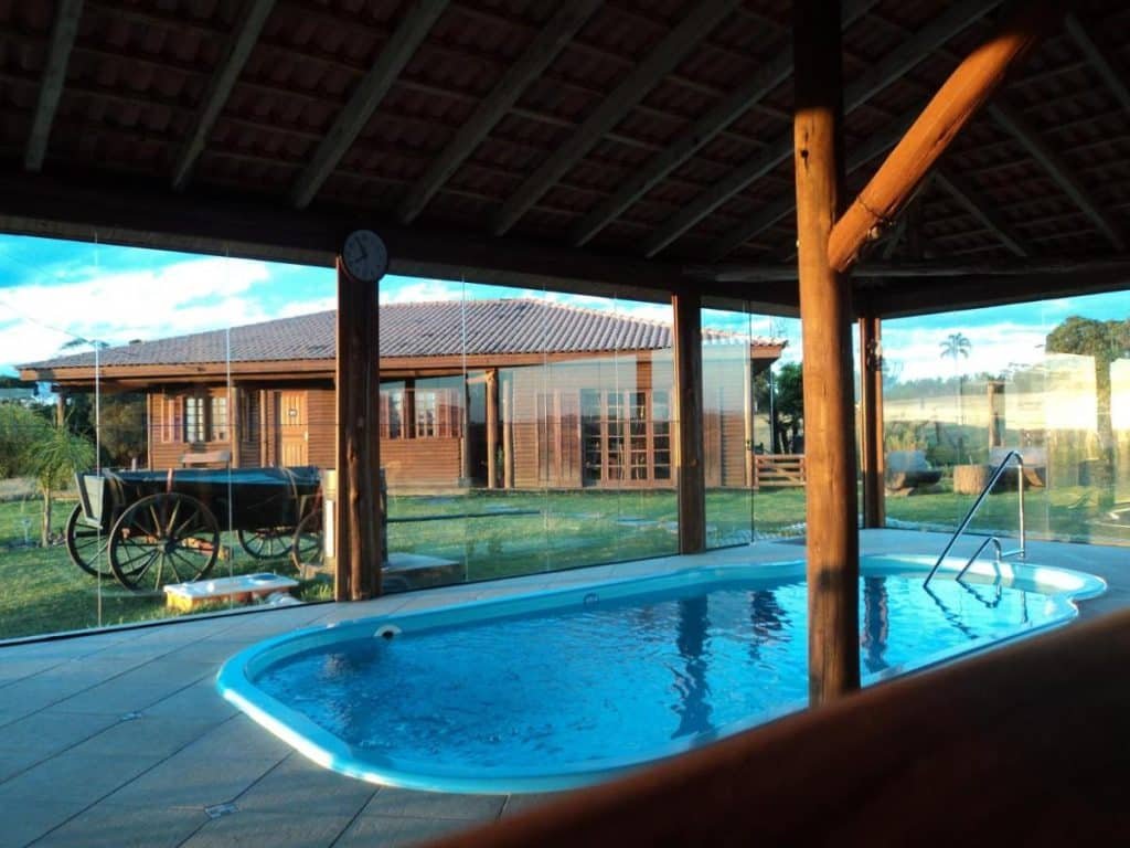 Piscina coberta do Hotel Fazenda e Pousada Rancho da Guaiaca. Parede de vidro com vista para o jardim.