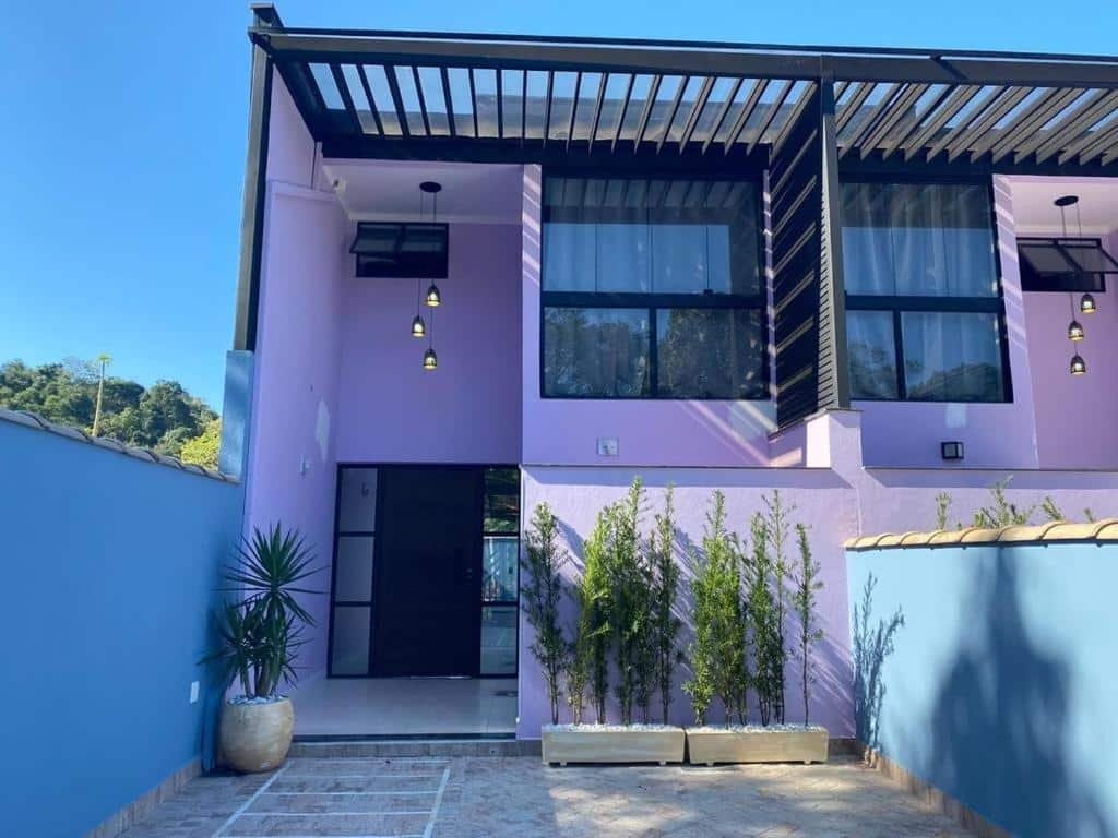 Frente do Recanto Bella Paraty. Uma casa com primeiro andar, na frente vasos de planta, no fundo a porta, em cima uma janela, do lado direito um muro com uma casa igual.