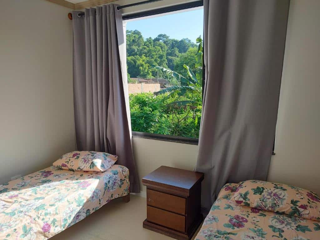 Quarto do Recanto Bella Paraty. Uma cama de solteiro de cada lado, uma cômoda no meio, no fundo uma janela com a cortina aberta.