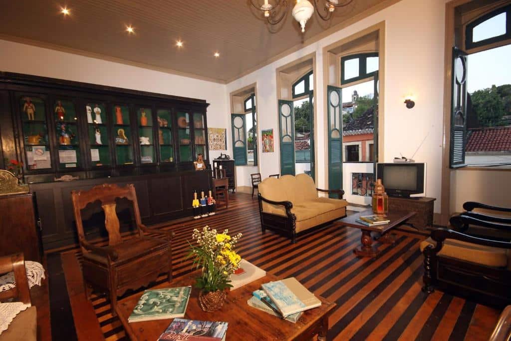 Poltronas e cadeiras, duas mesas de centro, uma pequena televisão. Um armário no fundo, e as paredes com grandes janelas com vista para a cidade.