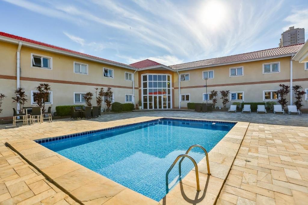Piscina do Red Roof Inn Jundiaí com um deck amplo ao redor com algumas plantas e espreguiçadeiras brancas, para representar hotéis perto do Hopi Hari