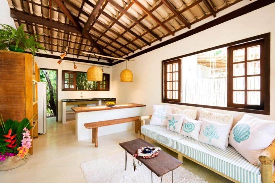 Sala de estar da Casa Mariane Trancoso com sofá do lado direito da imagem com uma mesa no centro da casal e ao fundo a cozinha.