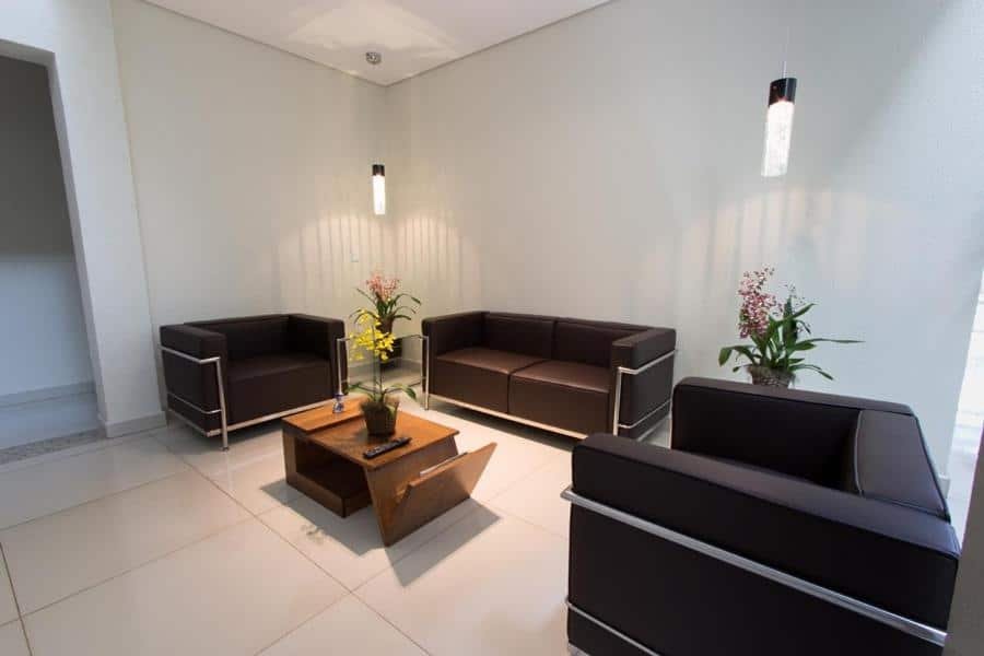 Sala de espera do Hotel Villa de Holanda com sofá de couro marrom, mesa de centro de madeira com vaso de flores em cima. Representa hotéis em Holambra.