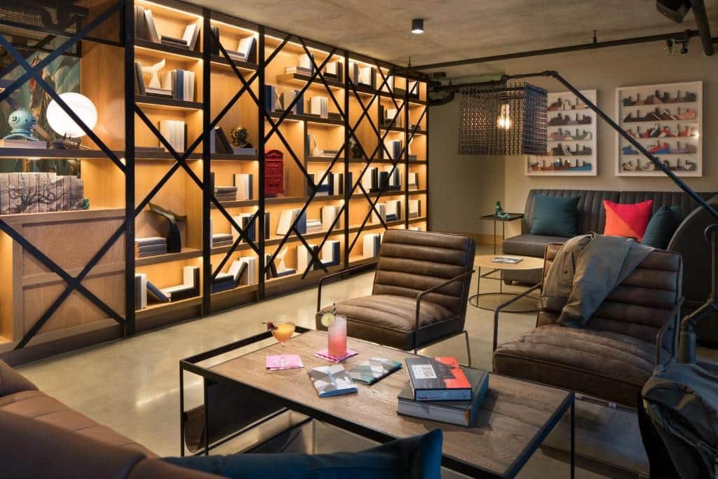 Sala do Moxy San Diego Gaslamp Quarter com cadeiras e mesa de centro e uma estante do lado esquerdo com livros. Representa hotéis em San Diesgo