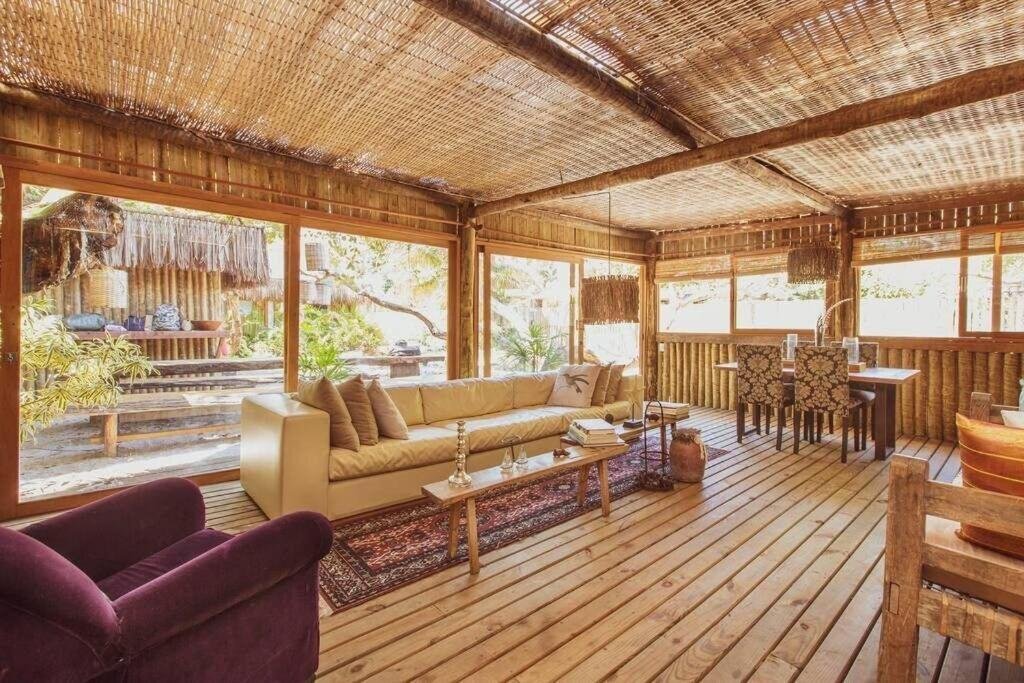 Sala de estar Vila Botanika Caraíva com poltrona do lado esquerdo da imagem a frente um sofá e uma mesa de centro, do lado esquerdo do sofá a frente uma mesa de madeira com quatro cadeiras.