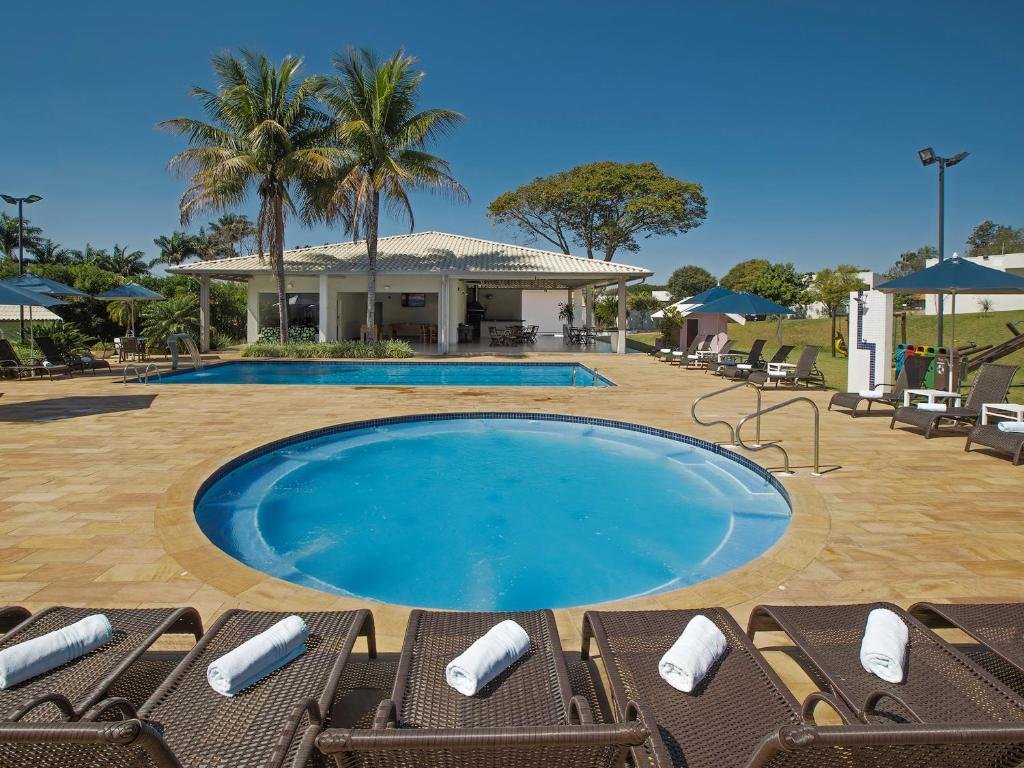 Piscina do Valinhos Plaza Hotel com um deck ao redor com algumas espreguiçadeiras, árvores e um gramado