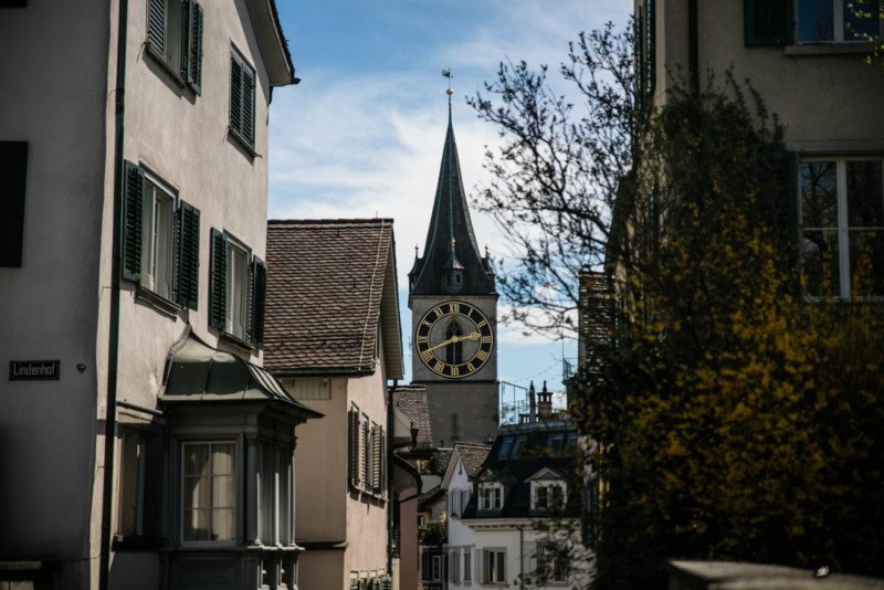 Imagem de casas do a frente durante o dia e ao fundo a torre da Igreja de São Pedro. Representa o que fazer em Zurique.